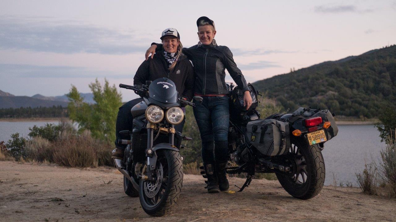 2 female motorcycle riders posing in front of lake