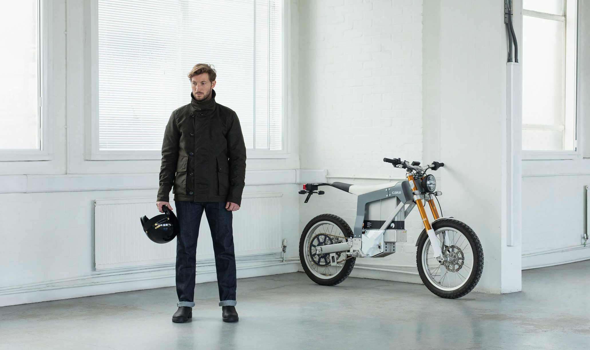 a model wearing the Ashley Watson Armoured Jacket for motorcyclists, next to what appears to be a motor scooter