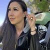 A woman rider inserting MOTO PRO ear plugs into her ear while sitting in front of a motorcycle.