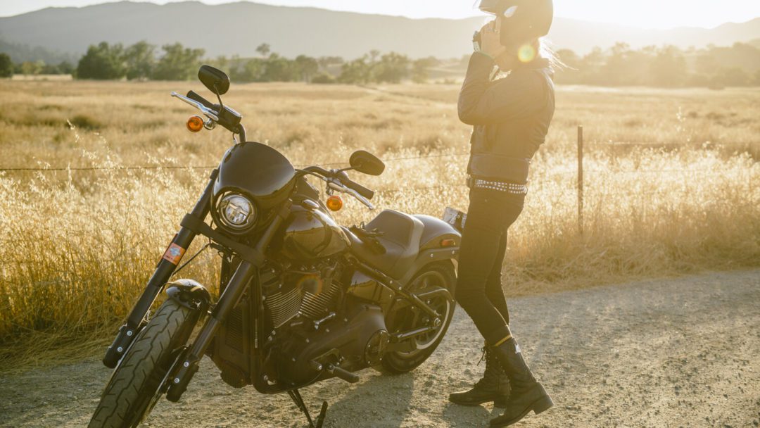 a view of a rider enjoying the tail-end of a ride, taking off her helmet in the sunset