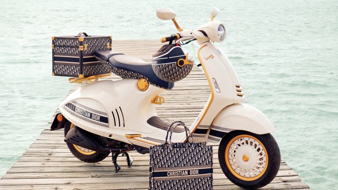 a side view of a 2012 Special Edition Christian Dior Vespa 946 on a dock with water in the background, and matching Dior helmet, bag, and back cartage.