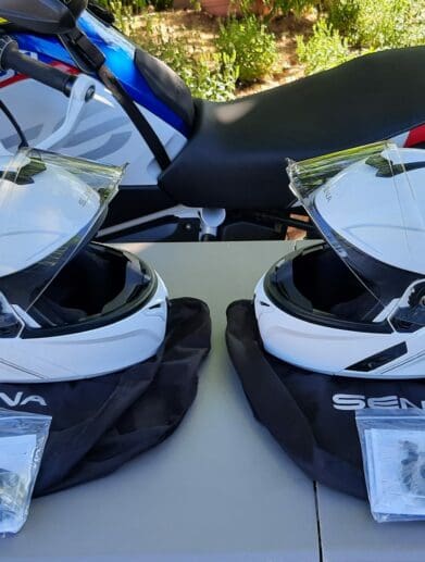 A view of two Outrush R Modular Helmets, in front of a BMW Motorcycle