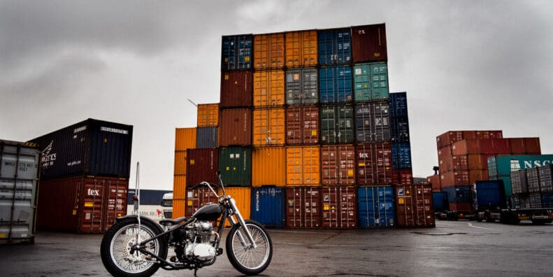Shipping containers behind a beautiful motorcycle, symbolic of the shipping container inflation rates present in today's post