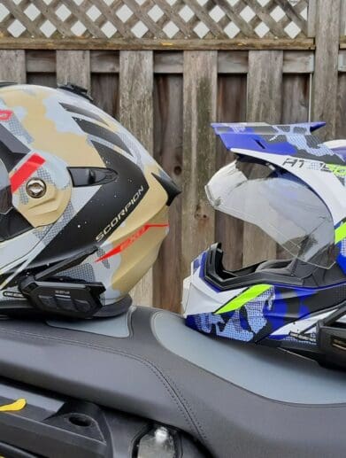 Sena SPIDER ST1 and RT1 mesh systems on two different helmets resting on motorcycle seat