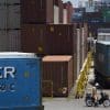 A worker sits on a scooter near shipping containers at a port in Shizuoka City, Shizuoka Prefecture, Japan, on Monday, June 27, 2016. Bank Of Japan Governor Haruhiko Kuroda has said lower interest rates are one of the goals of his policy mix of unprecedented asset purchases and a negative deposit rate, designed ultimately to drive inflation to 2 percent. Photographer: Tomohiro Ohsumi/Bloomberg