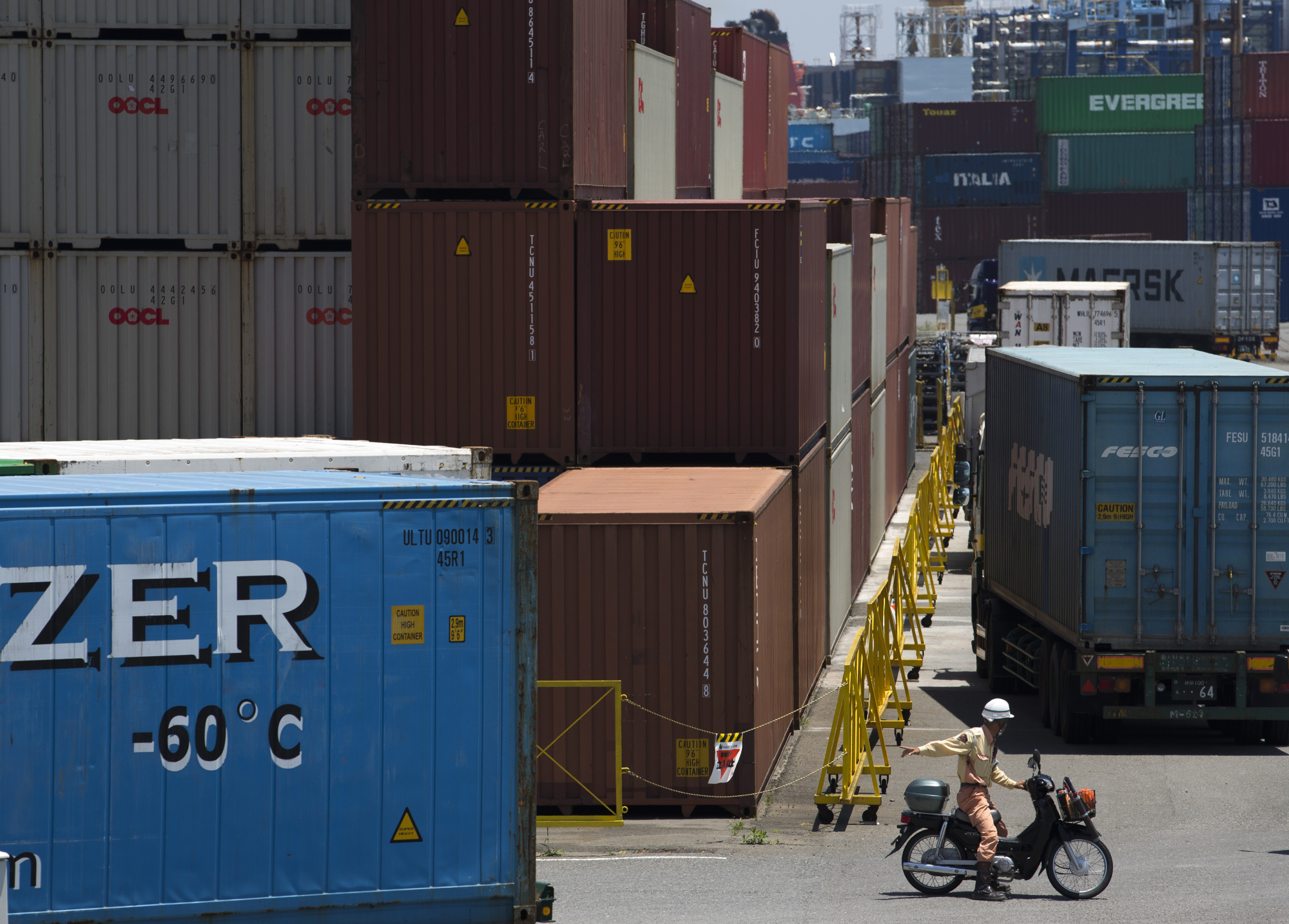 A worker sits on a scooter near shipping containers at a port in Shizuoka City, Shizuoka Prefecture, Japan, on Monday, June 27, 2016. Bank Of Japan Governor Haruhiko Kuroda has said lower interest rates are one of the goals of his policy mix of unprecedented asset purchases and a negative deposit rate, designed ultimately to drive inflation to 2 percent. Photographer: Tomohiro Ohsumi/Bloomberg