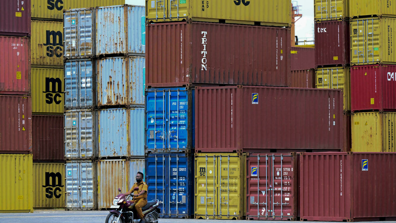 A worker sits on a scooter near shipping containers at a port 