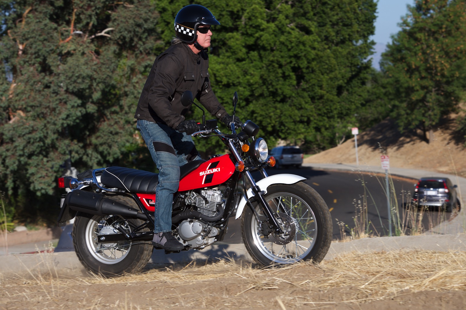 Man standing astride red and black Suzuki VanVan 200 near country road