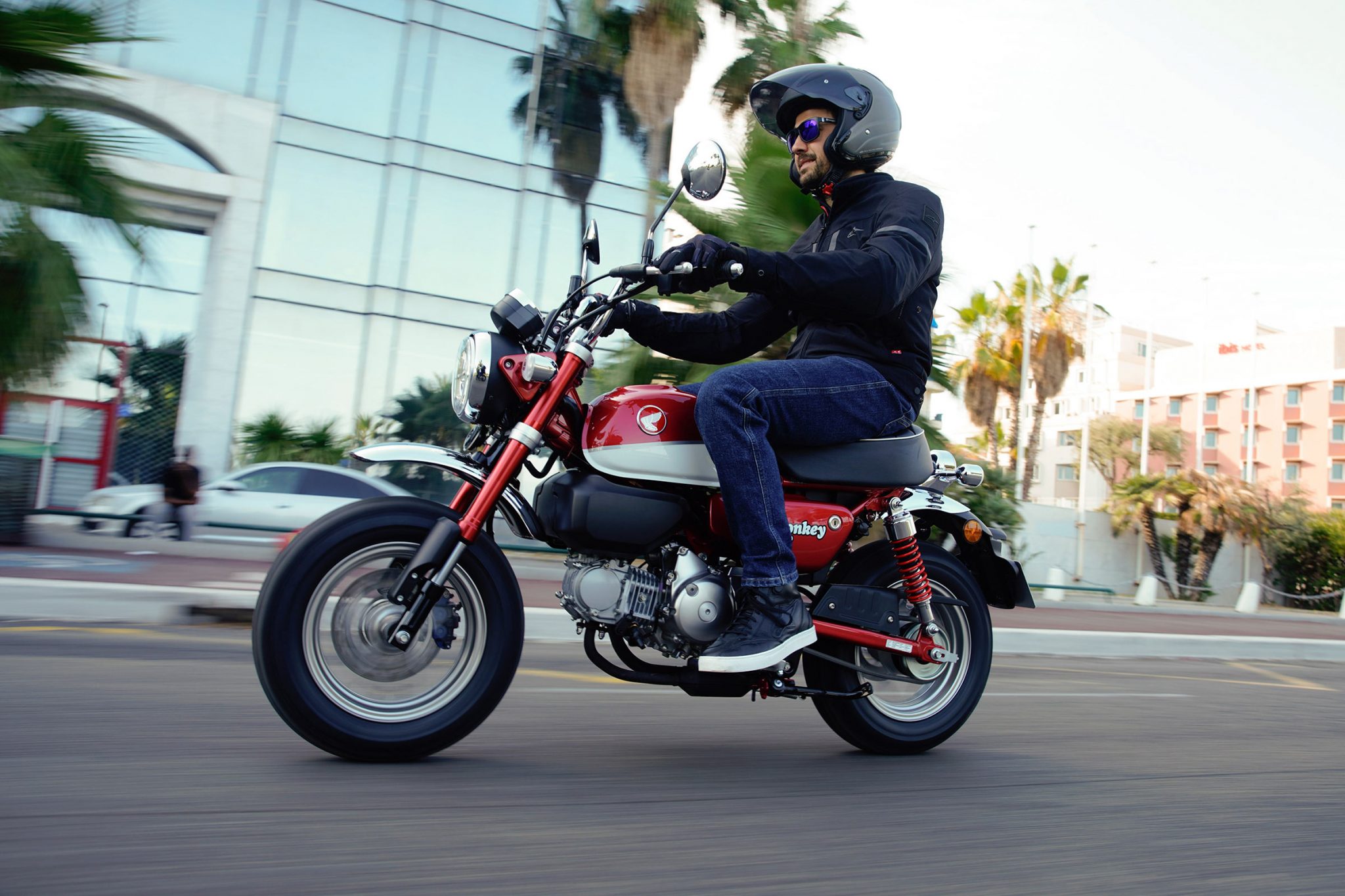 Rider on red Honda Monkey speeding down city street