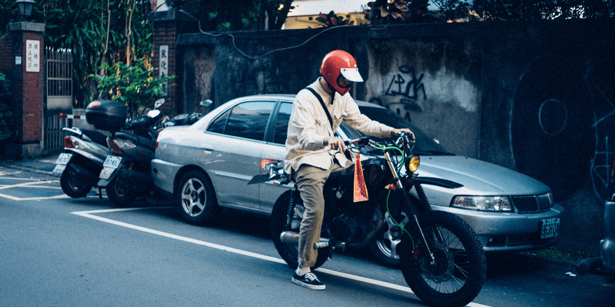 A side view of a motorcyclist next to a car