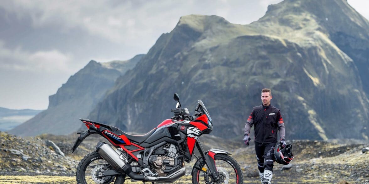A view of a Honda motorcycle and rider in a mountainous topography with grass and sun shining