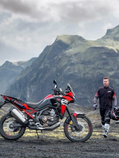 A view of a Honda motorcycle and rider in a mountainous topography with grass and sun shining