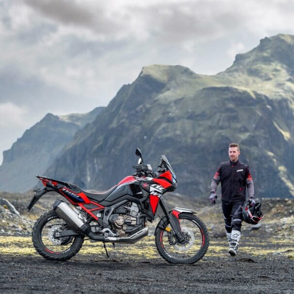 A view of a Honda motorcycle and rider in a mountainous topography with grass and sun shining