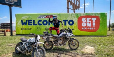 Rider posing on dirt bike in front of banner for GET ON Adv Fest by RevZilla