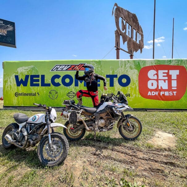 Rider posing on dirt bike in front of banner for GET ON Adv Fest by RevZilla