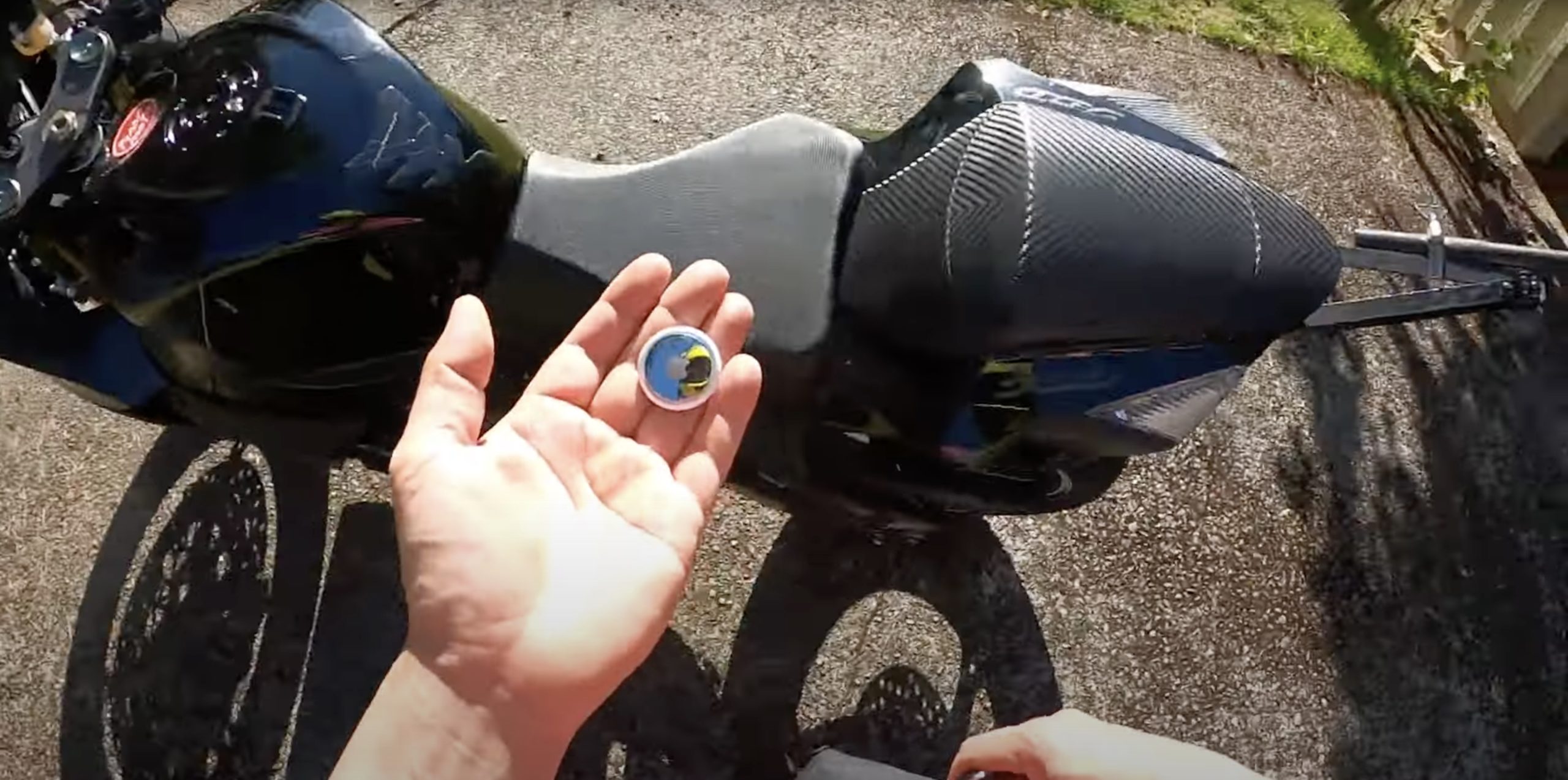 A hand holding an Apple AirTag to see fi it would be sufficient use as a locator for moto anti-theft