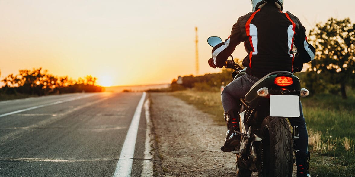 Female student with helmet taking motorcycle lessons and practicing ride. In background traffic cones and instructor with checklist rating and evaluating the ride. Motorcycle school of driving.