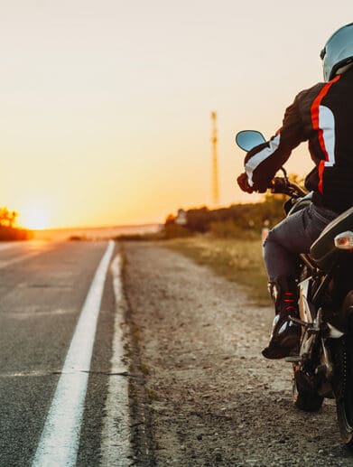 Female student with helmet taking motorcycle lessons and practicing ride. In background traffic cones and instructor with checklist rating and evaluating the ride. Motorcycle school of driving.