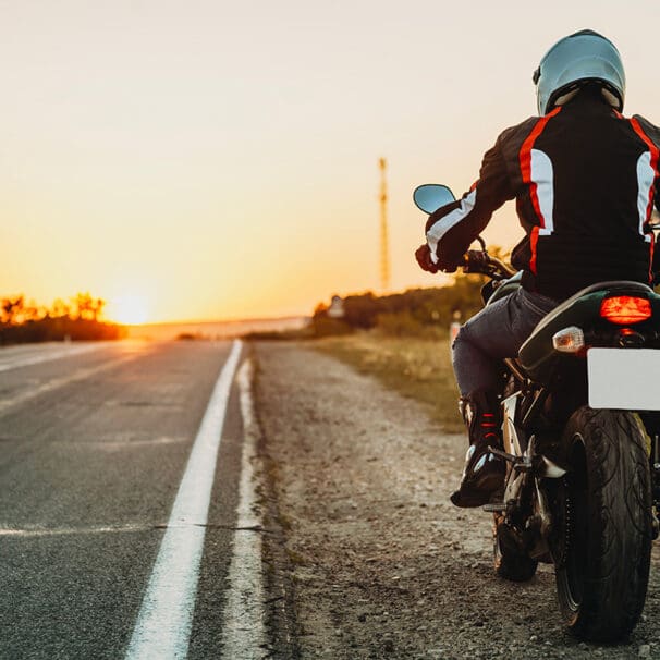 Female student with helmet taking motorcycle lessons and practicing ride. In background traffic cones and instructor with checklist rating and evaluating the ride. Motorcycle school of driving.