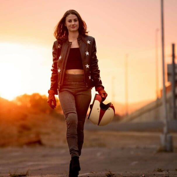 Woman in motorcycle riding pants walking through desert