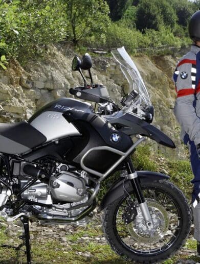 A Beemer dismounted from his BMW and standing in front of a wall of green foliage. Media sourced from Beach Moto.