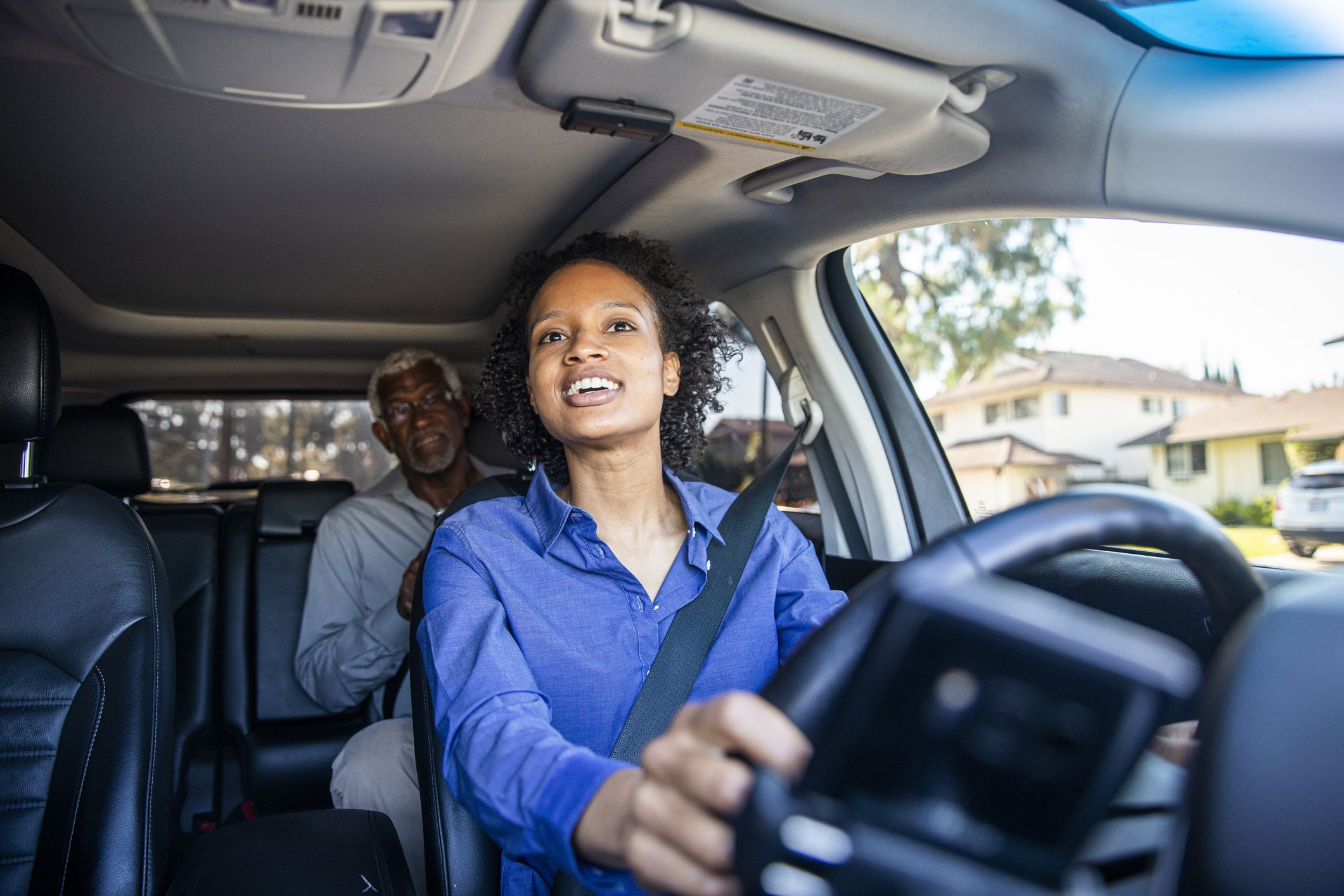 A woman driving a car with a man in the back seat. Media sourced from Car and Driver.