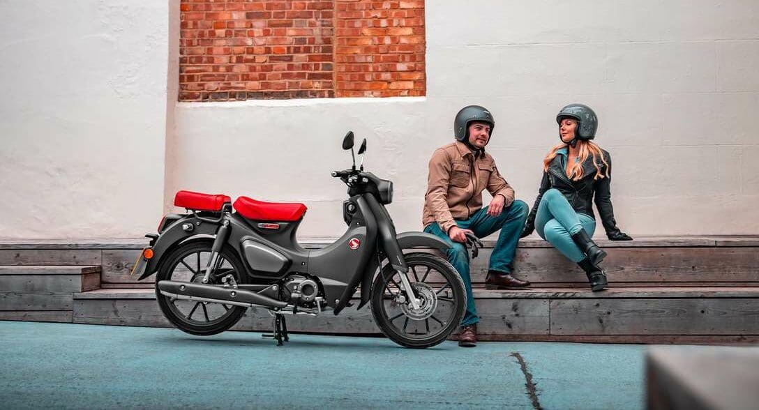 Two riders sitting near Honda Super Cub