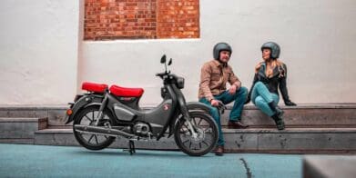 Two riders sitting near Honda Super Cub