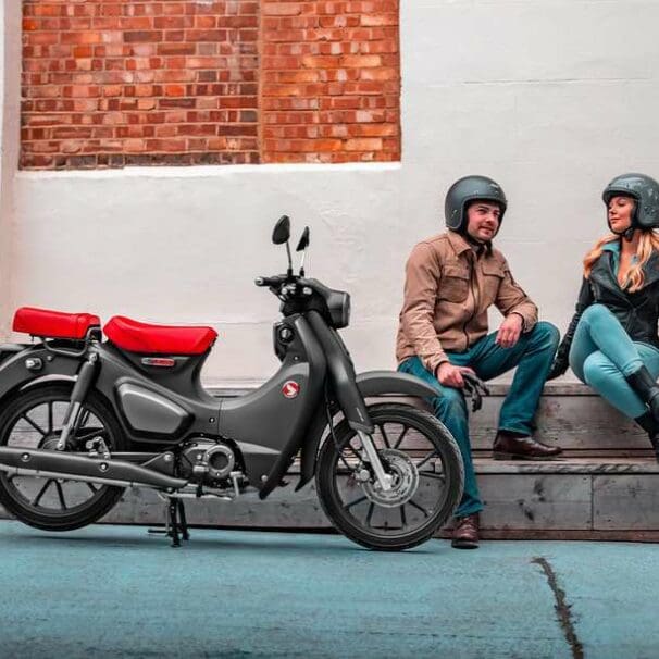 Two riders sitting near Honda Super Cub