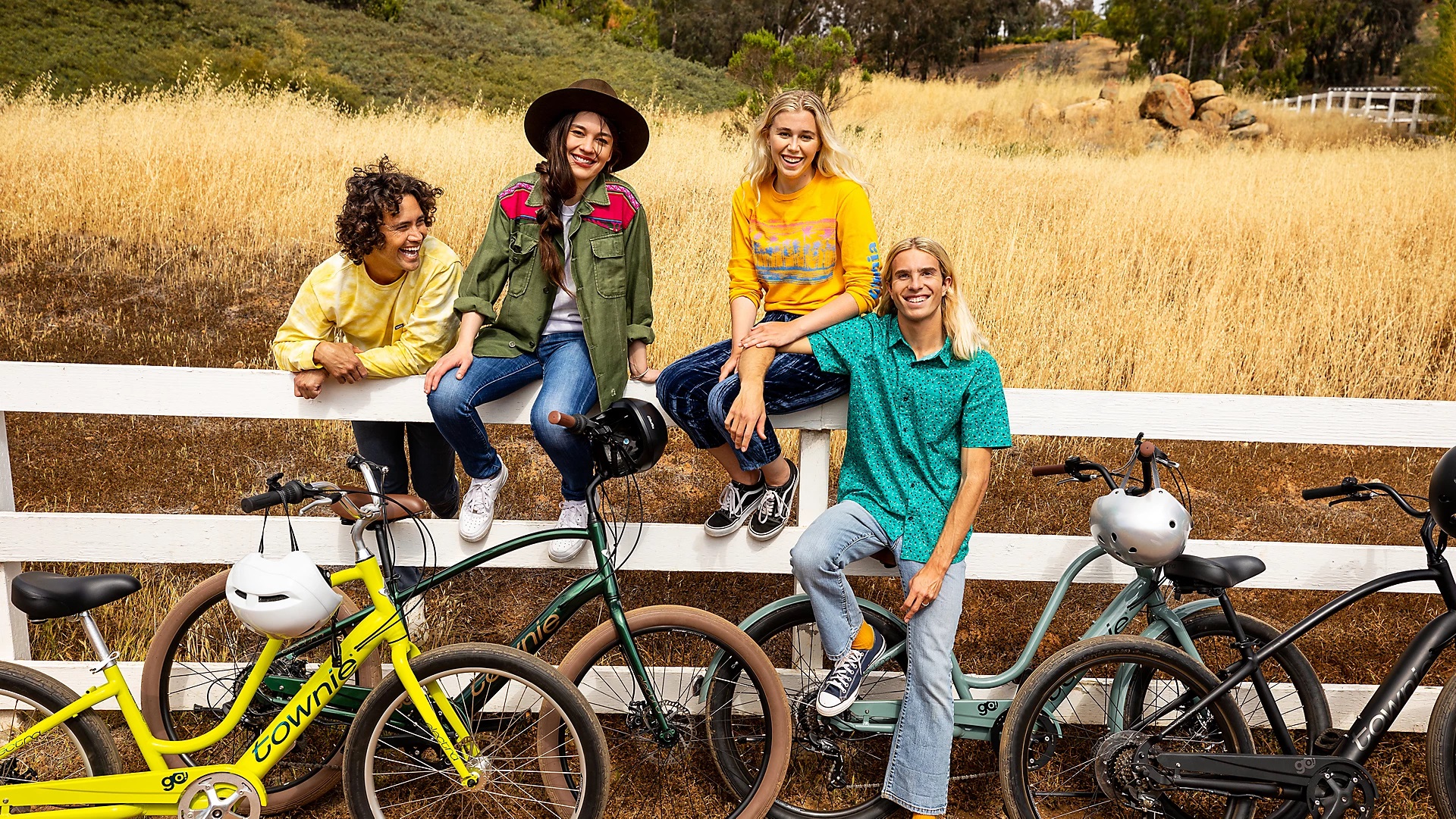 Group of friends sit on fence near several Electra electric bicycle models
