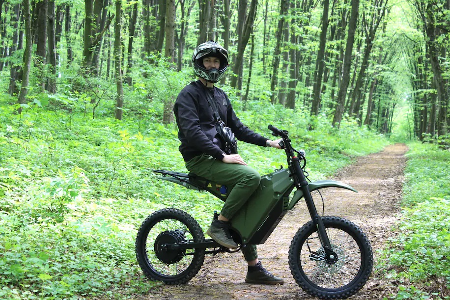 Helmeted rider on forest trail sits stationary on electric dirt bike during daytime