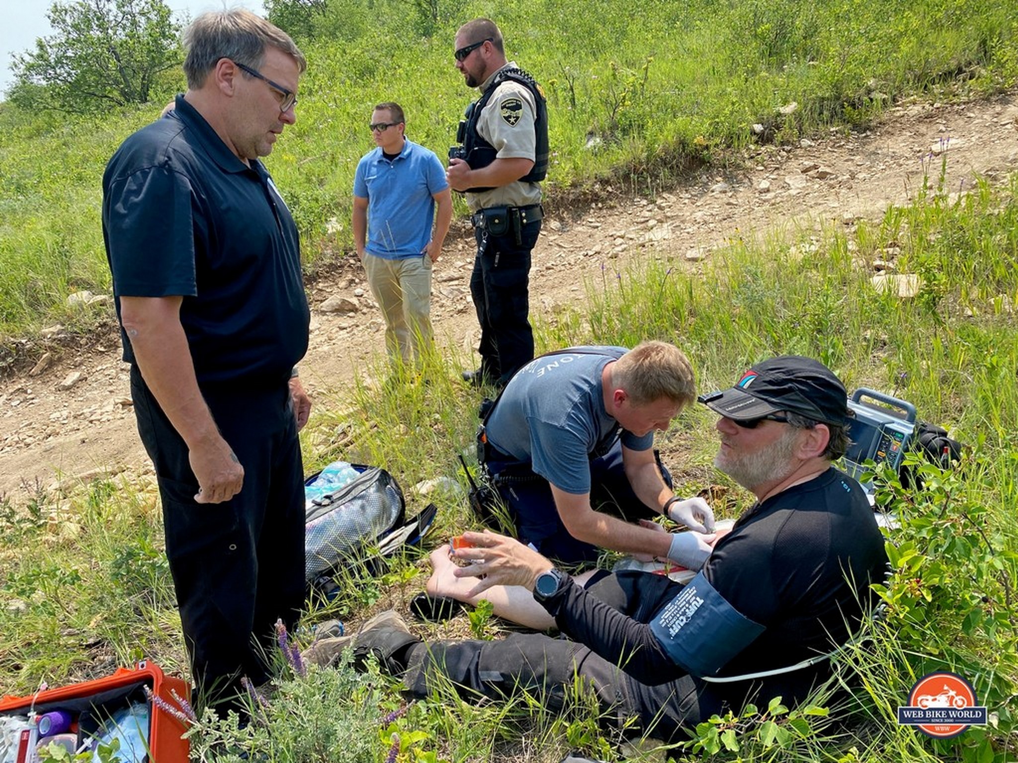 Man with broken ankle sitting down in grass while receiving medical care