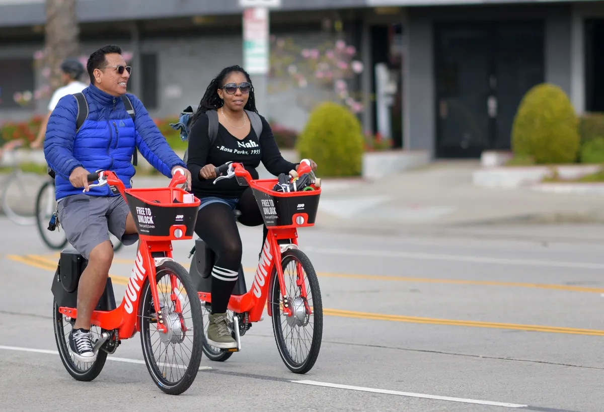 A man and a woman riding Jump ebikes on a public street.