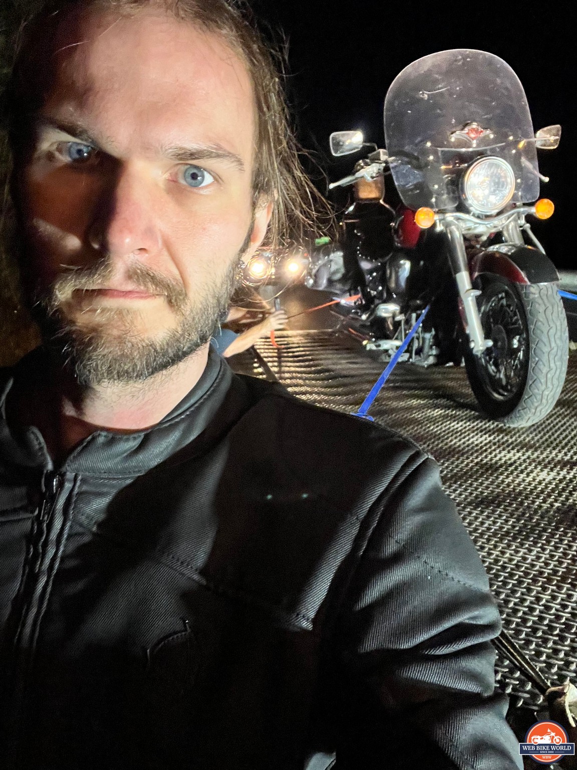 Author looking annoyed as motorcycle is lifted onto flatbed truck in background