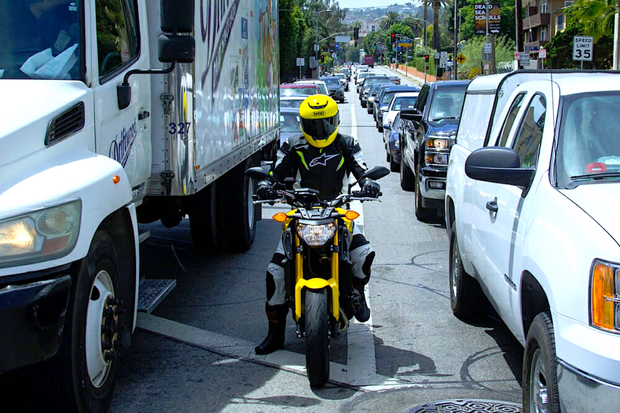 A rider lane filtering as cars wait at a stopped light. Media sourced from Cycle News.