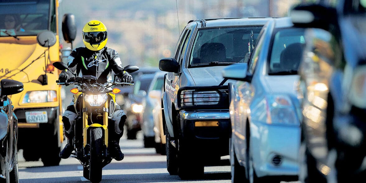 A rider lane filtering as cars wait at a stopped light. Media sourced from Rider Magazine.