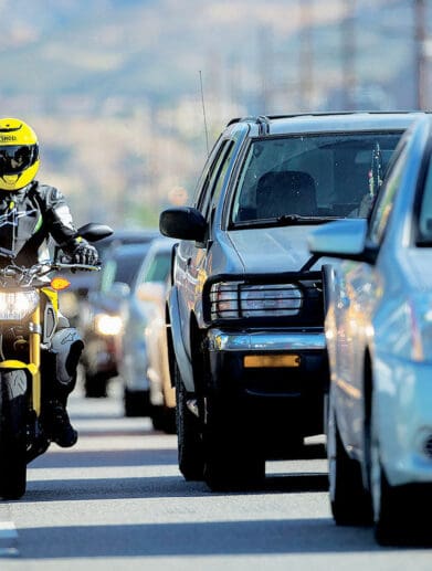 A rider lane filtering as cars wait at a stopped light. Media sourced from Rider Magazine.
