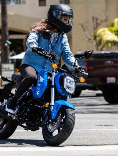 Woman riding small blue Honda Grom on city street