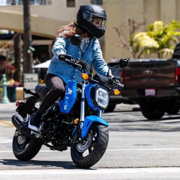 Woman riding small blue Honda Grom on city street
