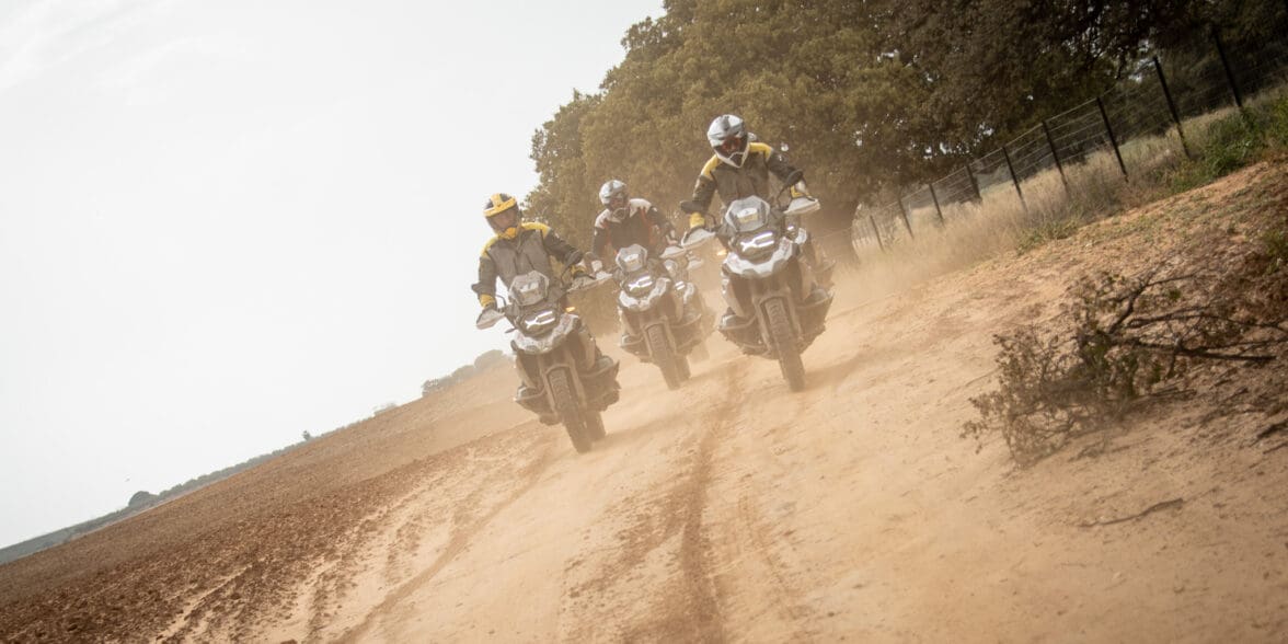 A head-on image of three riders on BMW motorcycles riding on a dirt road.