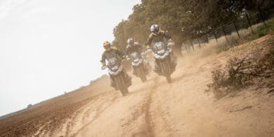 A head-on image of three riders on BMW motorcycles riding on a dirt road.