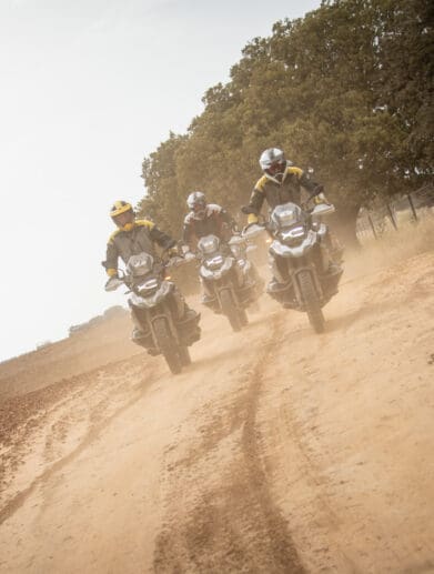 A head-on image of three riders on BMW motorcycles riding on a dirt road.