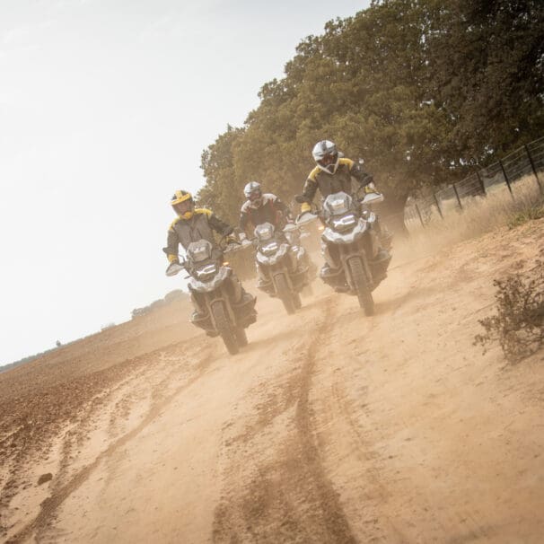 A head-on image of three riders on BMW motorcycles riding on a dirt road.