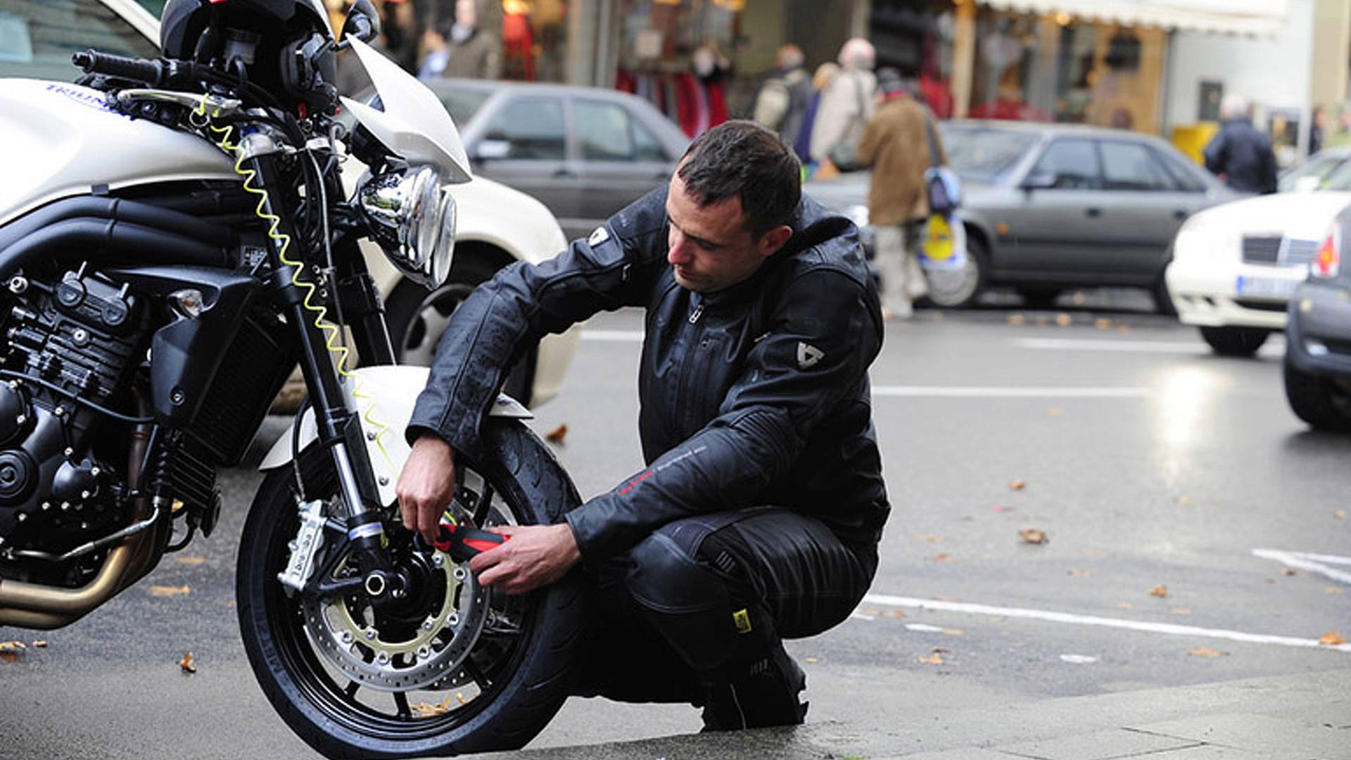 A rider securing a bike lock on the front wheel. Media sourced from RideApart.