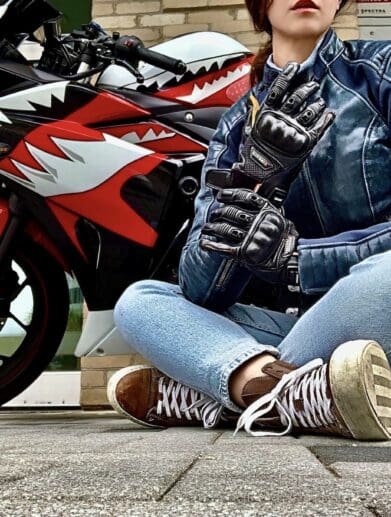 Author sitting cross-legged in front of motorcycle while wearing the Racer USA Women's Pitlane Gloves