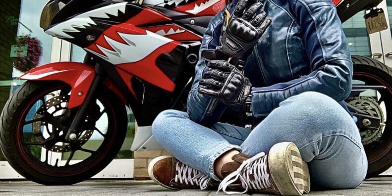 Author sitting cross-legged in front of motorcycle while wearing the Racer USA Women's Pitlane Gloves