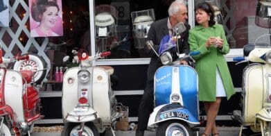 An old Italian couple next to a lineup of classic Vespa scoots. Media sourced from The Guardian.