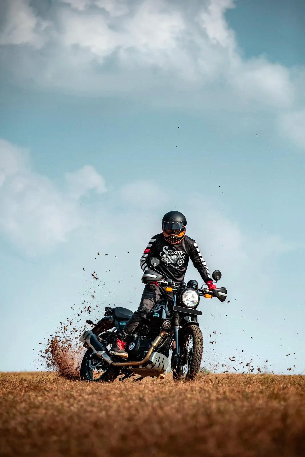 A 2022 Royal Enfield Scram 411 motorcycle kicks up some dirt in a field