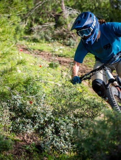 Mountain biker wearing helmet and goggles rides down a rough forest trail during daytime