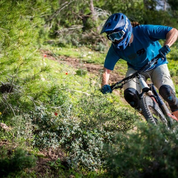 Mountain biker wearing helmet and goggles rides down a rough forest trail during daytime